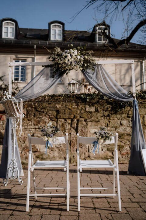 Eleganter mobiler Hochzeitsempfang mit weiß dekorierten Stühlen und Blumenschmuck vor historischem Gebäude