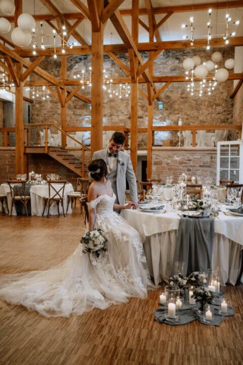 Brautpaar in festlichem Hochzeitssaal mit hölzernen Balkendecken, geschmückten Tischen und stimmungsvoller Beleuchtung