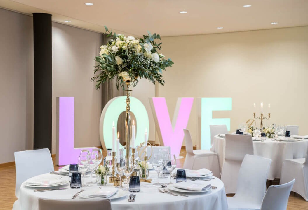 Elegante Hochzeitstafel mit leuchtendem LOVE-Schriftzug und exquisiter Blumendekoration