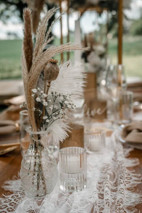 Elegante Tischdekoration für eine Hochzeit mit Trockenblumen und Sektgläsern auf Spitzen-Tischläufer
