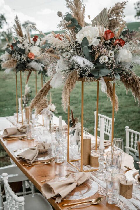 Elegante Hochzeitstafel mit goldenen Ständern für üppige Blumenarrangements und raffinierte Tischdekoration im Freien