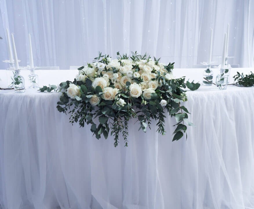 Elegantes Hochzeitstischarrangement mit weißer Blumendekoration und Kerzen