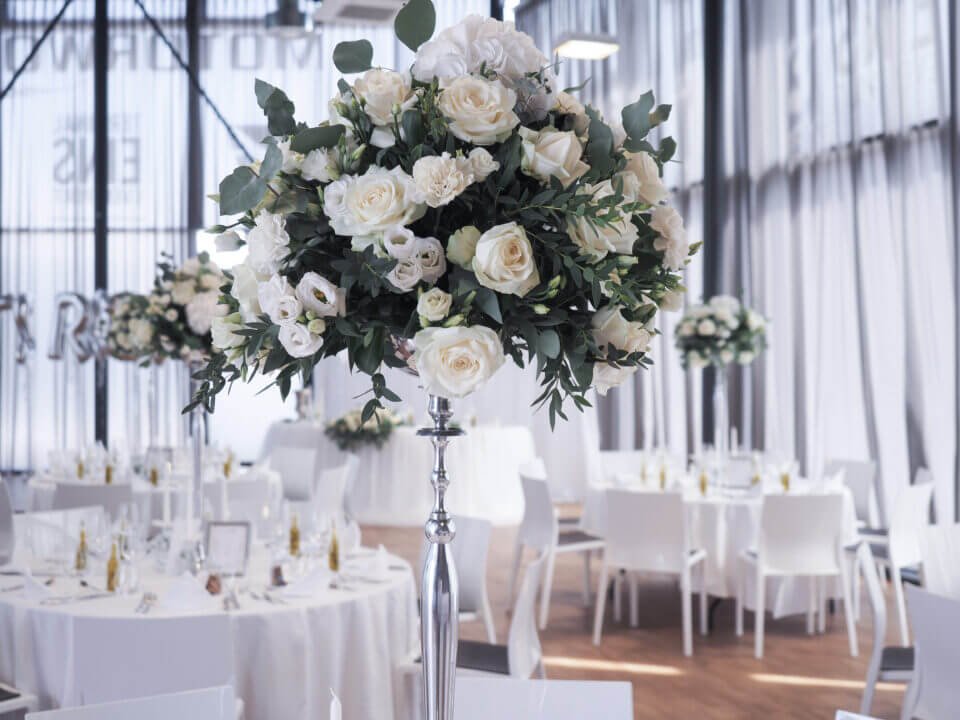 Eleganter Hochzeitssaal dekoriert mit weißen Rosenarrangements und festlich gedeckten Tischen für eine Hochzeitsfeier