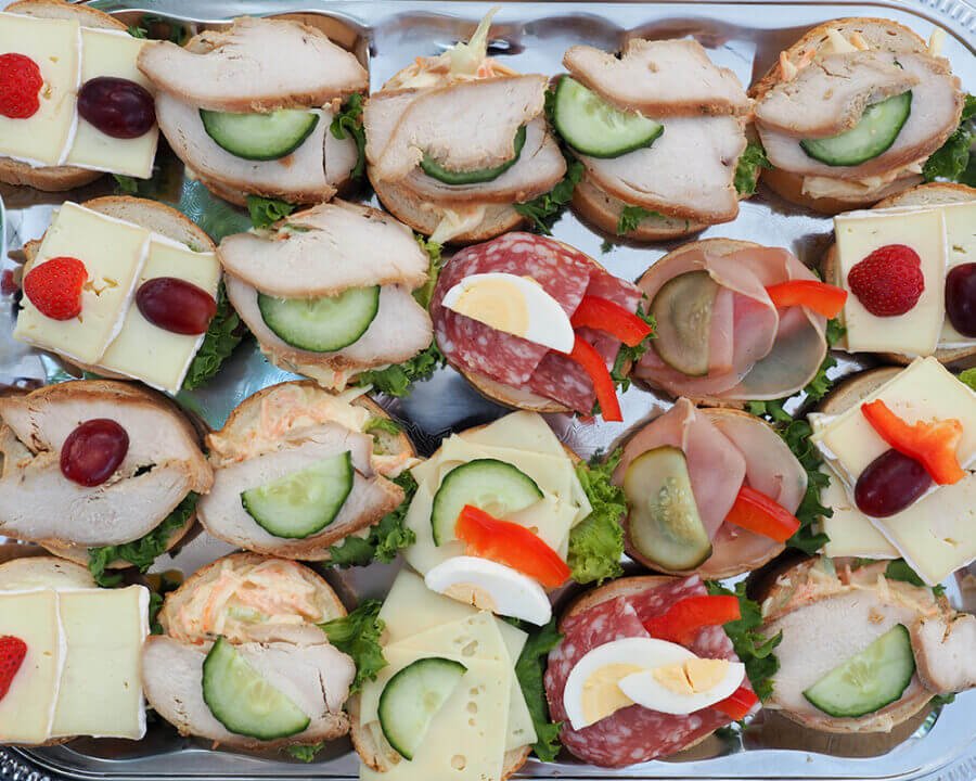Verschiedene belegte Brötchen auf einem Tablett, angerichtet für einen mobilen Sektempfang