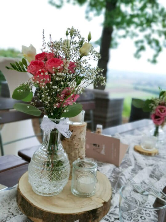 Blumengesteck auf Hochzeitstisch mit rustikaler Dekoration im Freien